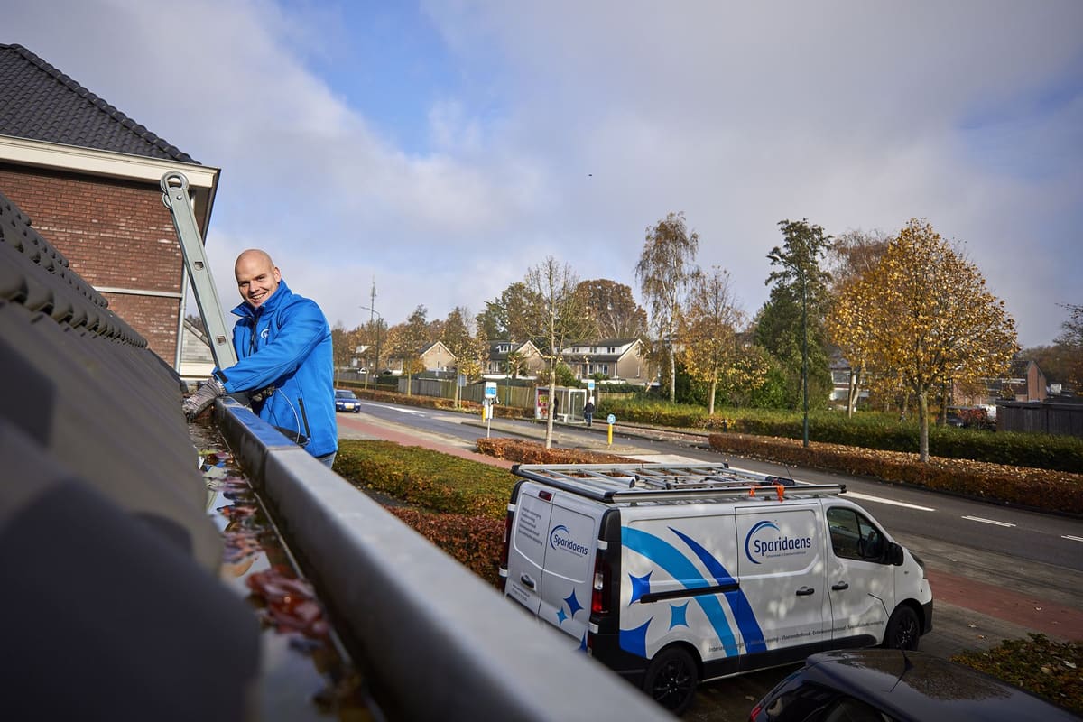 Bladafval en vuil dat met de hand uit een verstopte dakgoot wordt gehaald