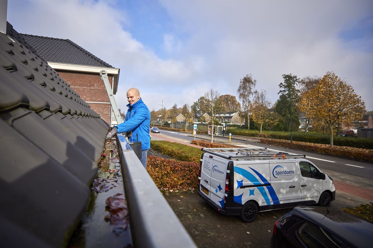 Medewerker van Sparidaens maakt een dakgoot met de hand schoon